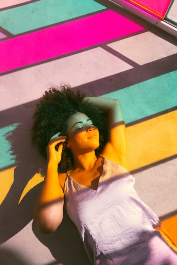 Woman relaxing on a colorful sunlit floor with shadows creating vibrant patterns.